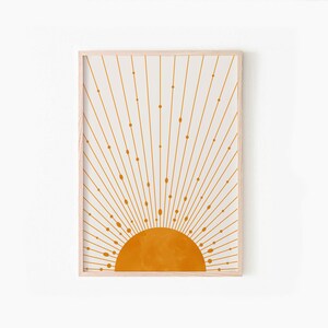 May include: A framed print of a minimalist sun design with a yellow sun and white rays on a cream background.