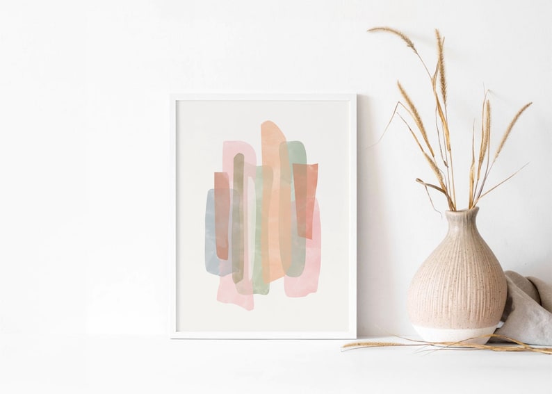 May include: Abstract art print with a white frame. The print features a design of overlapping shapes in shades of pink, peach, green, and brown.
