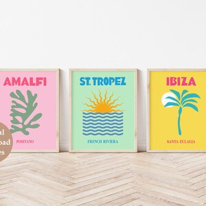 May include: Three framed prints with a minimalist design. The first print is pink with a green leaf and the text "Amalfi Positano". The second print is light green with a blue and white wave and a yellow sun with the text "St. Tropez French Riviera". The third print is yellow with a blue palm tree and the text "Ibiza Santa Eulalia".