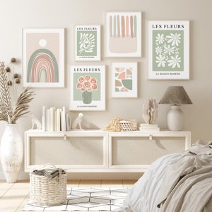 May include: Five minimalist art prints with a bohemian theme. The prints feature abstract shapes, flowers, and a rainbow in muted tones of green, pink, and white. The prints are displayed on a white wall above a white dresser.