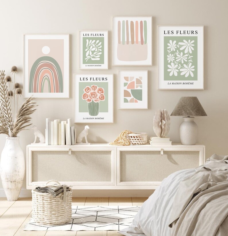 May include: Five minimalist art prints with a bohemian theme. The prints feature abstract shapes, flowers, and a rainbow in muted tones of green, pink, and white. The prints are displayed on a white wall above a white dresser.