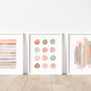 May include: Set of three abstract watercolor prints in muted pink, green, and brown tones. The prints feature geometric shapes and lines.