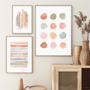 May include: Three abstract watercolor prints in muted tones of pink, orange, and green. The prints feature geometric shapes and lines.