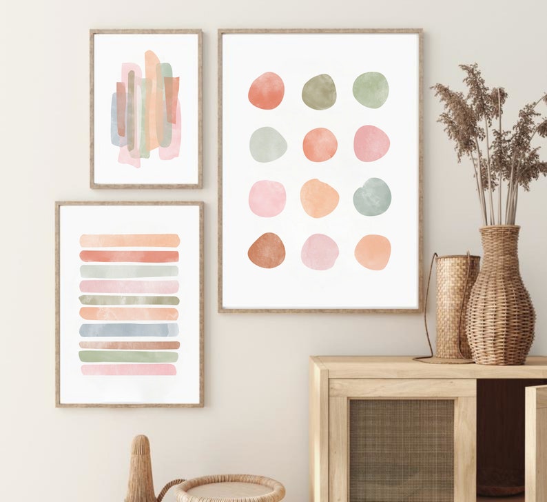 May include: Three abstract watercolor prints in muted tones of pink, orange, and green. The prints feature geometric shapes and lines.