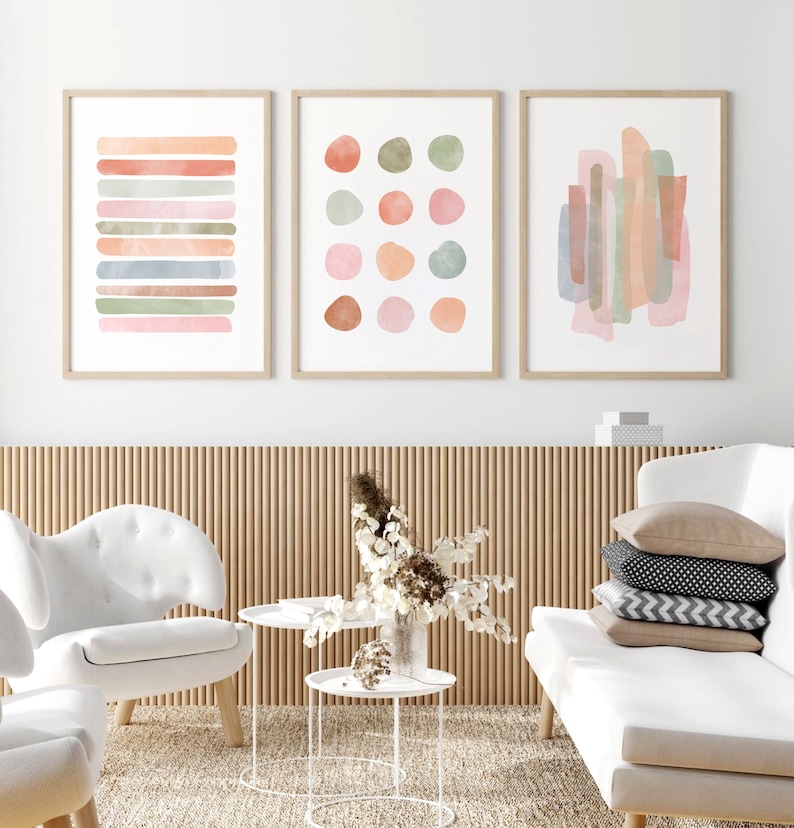 May include: Three framed abstract watercolor paintings with a neutral color palette of pink, green, and brown. The paintings are hung on a white wall above a wooden slat wall.