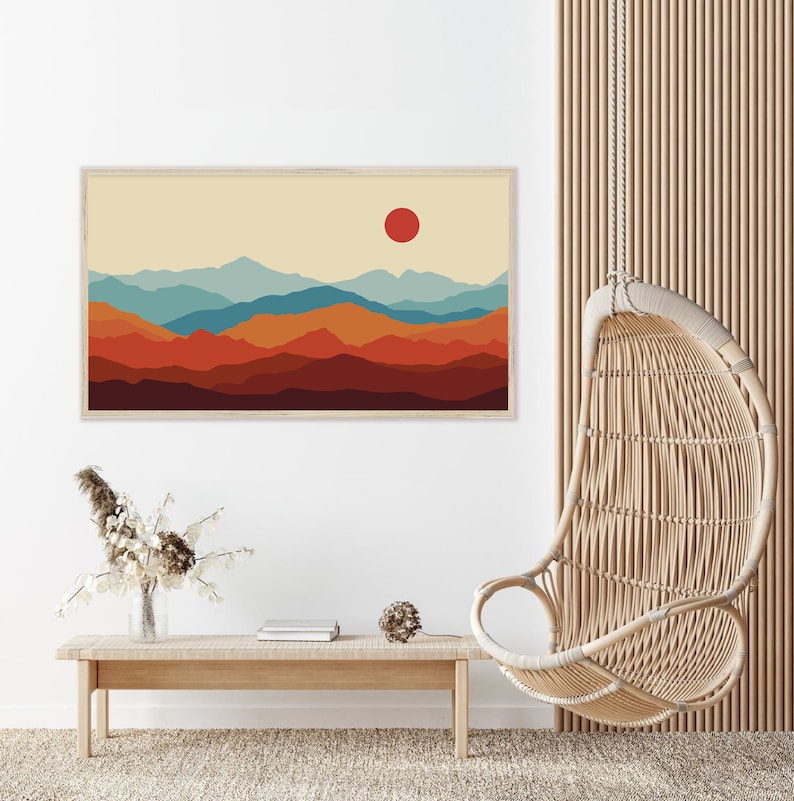 K&ouml;nnte beinhalten: Ein digitaler Kunstdruck einer Bergkette mit einer roten Sonne am Himmel. Die Berge sind in Blaut&ouml;nen, Orange und Braun geschichtet. Der Druck ist in einem hellen Holzrahmen gerahmt.
