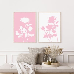 May include: Two framed prints with white silhouettes of roses on a pink and white background. The prints are hanging on a white wall above a couch with a throw blanket and pillows.