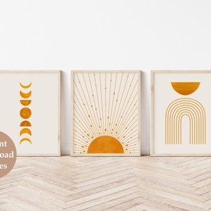 May include: Three minimalist wall art prints with a white background and gold geometric shapes. The first print features a series of crescent moons, the second print features a sun with rays, and the third print features a half circle and an arch.