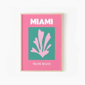 May include: A pink and teal poster with the text "MIAMI" and "MIAMI BEACH" in white. A stylized pink coral design is in the center of the poster.