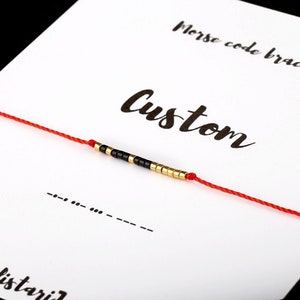 Peut inclure: Un bracelet en cordon rouge avec des perles noires et dorées. Le bracelet est sur une carte blanche avec le texte "Bracelet code morse" et "Custom" écrit à l'encre noire. La carte comporte également une ligne de tirets et de points représentant le code morse.
