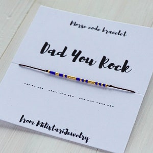 Peut inclure: Un bracelet en perles bleues et dorées avec le message "Dad You Rock" en code Morse sur une carte blanche. La carte indique également "Bracelet en code Morse" et "de Milistariejewelry".