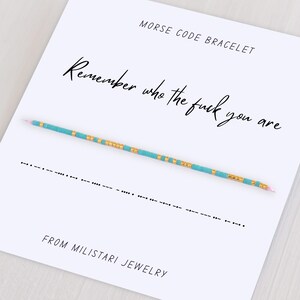 May include: A white card with the text "MORSE CODE BRACELET" and "Remember who the fuck you are." A turquoise and gold beaded bracelet is displayed. The bottom of the card reads "FROM MILISTARI JEWELRY."
