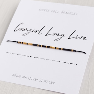 May include: A black and gold bracelet with the message "Cowgirl Long Live" in Morse code. The bracelet is displayed on a white card with the text "Morse Code Bracelet" and "From Miliatari Jewelry".