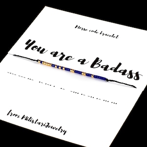 May include: A blue and gold beaded bracelet with the message "You are a badass" on a white card. The card also says "Morse code bracelet" and "from Militarijewelry".