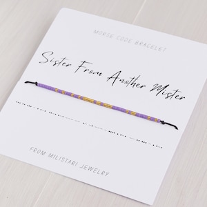 May include: A purple and gold beaded bracelet with a black string. The card reads "Morse Code Bracelet" and "Sister From Another Mister" in cursive. The card also reads "From Miliatari Jewelry".