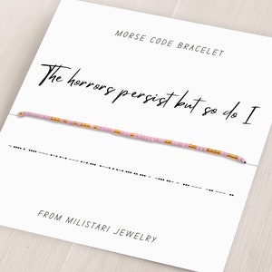 May include: A pink and gold beaded bracelet with the text "The horrors persist but so do I" and the morse code translation below. The bracelet is on a white card with the text "Morse Code Bracelet" and "From Miliatari Jewelry".