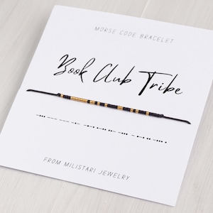 May include: A black and gold beaded bracelet with the words "Book Club Tribe" written in cursive on a white card. The bracelet is a Morse code bracelet with the code for "Book Club Tribe" written below the bracelet. The card also says "Morse Code Bracelet" and "From Miliatari Jewelry".