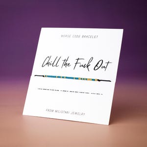 May include: A white card with the text "Chill the Fuck Out" and a Morse code bracelet. The bracelet has blue and gold beads. The card also says "Morse Code Bracelet" and "From Militari Jewelry".