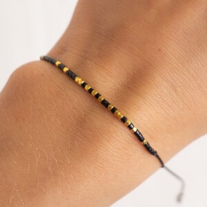 May include: A simple black and gold beaded bracelet with a sliding knot closure.