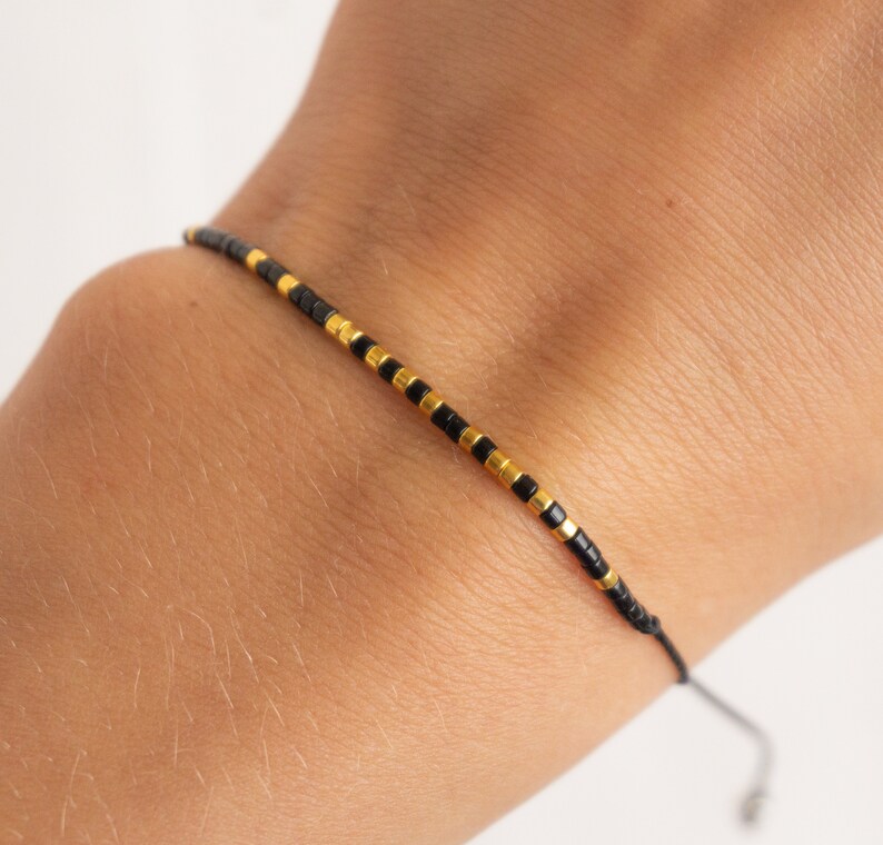 May include: A simple black and gold beaded bracelet with a sliding knot closure.