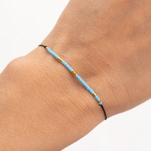 May include: A simple bracelet with light blue and gold beads on a black string.