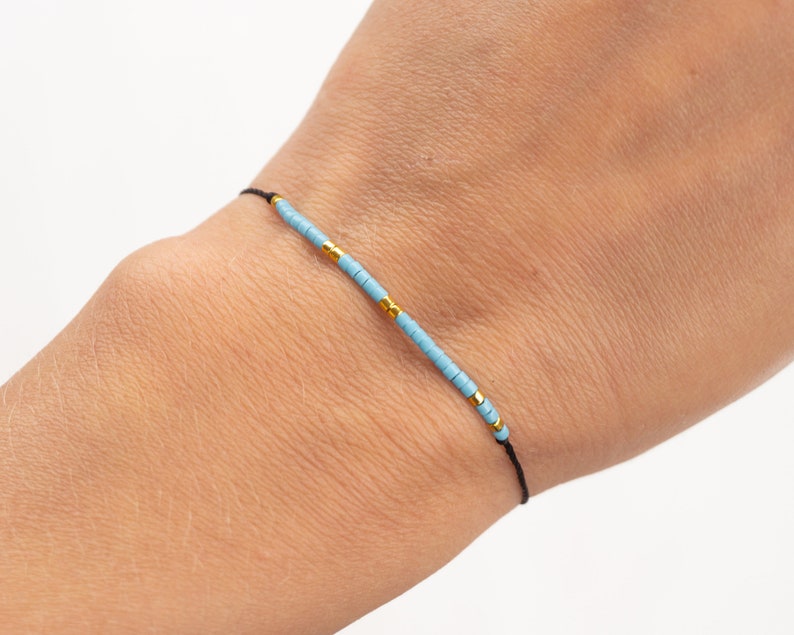 May include: A simple bracelet with light blue and gold beads on a black string.