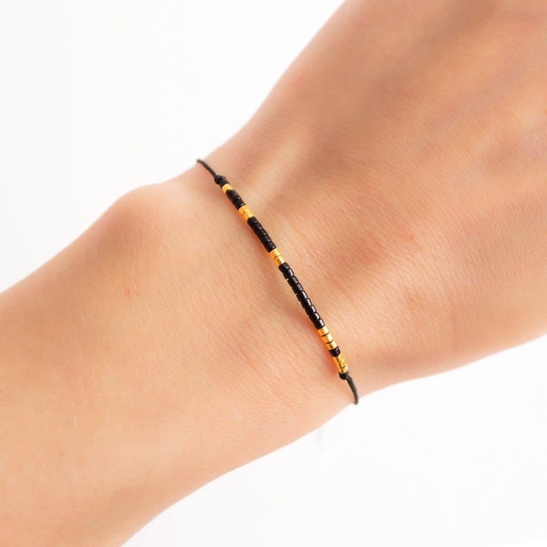 May include: A simple bracelet with black and gold beads on a black string.