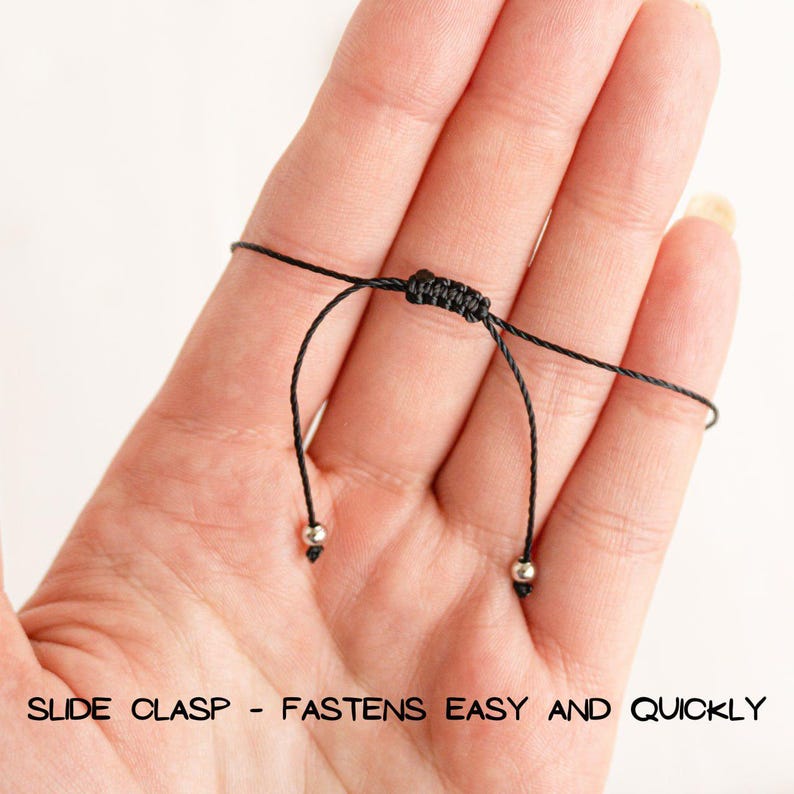 May include: A black cord bracelet with a slide clasp closure. The clasp is made of two small silver beads. "Slide Clasp - Fastens Easy and Quickly" is written below the bracelet.