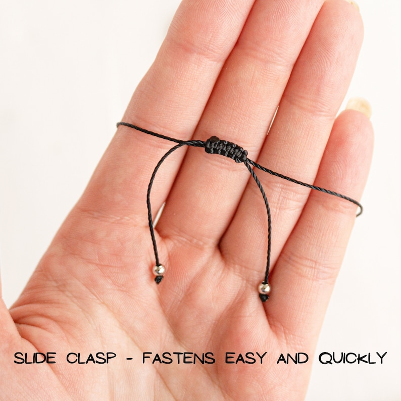 May include: Close-up of a black adjustable cord bracelet with silver beads and a slide clasp. "SLIDE CLASP - FASTENS EASY AND QUICKLY" is printed on the bottom of the image.