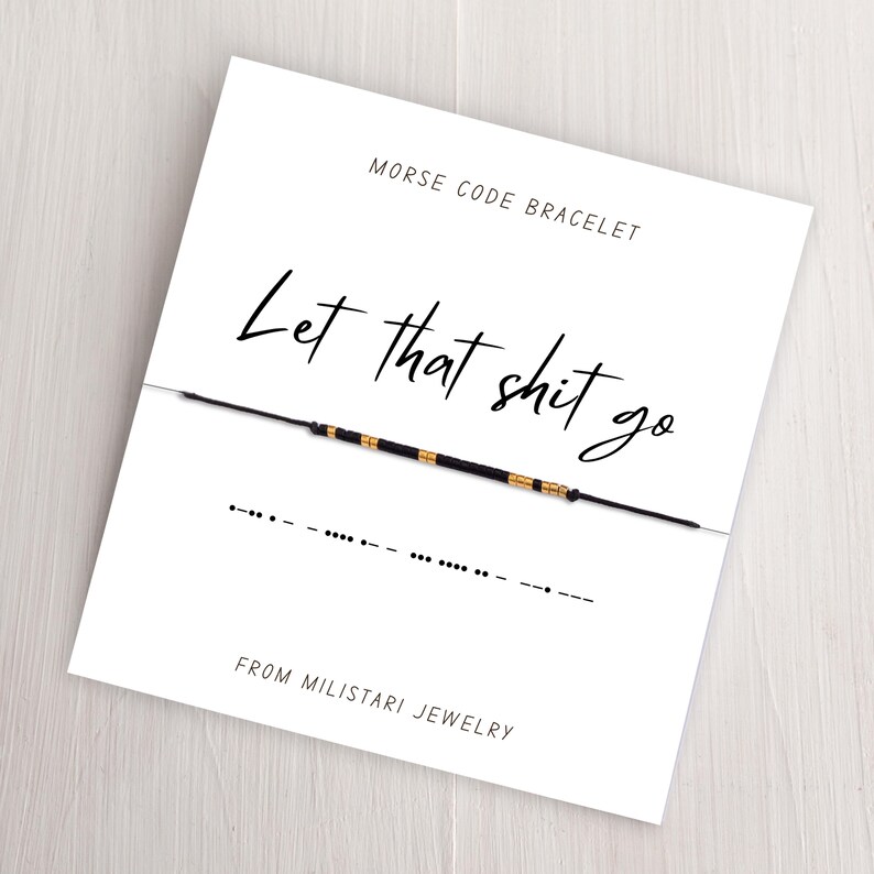 May include: A white card with black text that reads "Morse Code Bracelet" and "Let that shit go". The card also includes a black string bracelet with gold beads and the Morse code for the phrase.