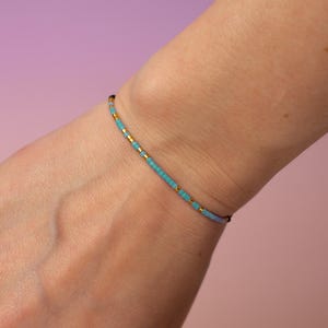 May include: A delicate bracelet made with small turquoise and gold beads. The bracelet is on a person's wrist.