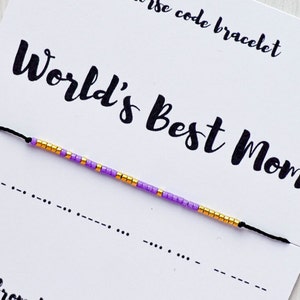 Peut inclure: Un bracelet d'amitié en perles violettes et dorées avec un cordon noir. Le bracelet est sur une carte blanche avec le texte "World's Best Mom".