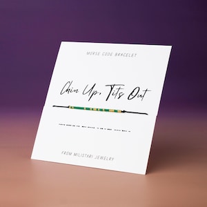 May include: A white card with the text "Chin Up, Tits Out" and a Morse code bracelet. The bracelet is black with green and gold beads. The card also says "Morse Code Bracelet" and "From Militari Jewelry".