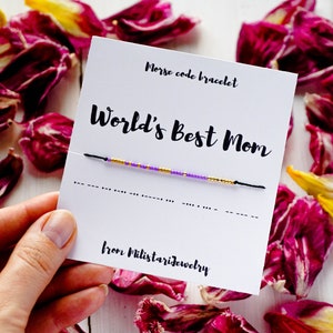 Peut inclure: Un bracelet en perles violettes et dorées avec un cordon noir. Le bracelet est sur une carte blanche avec le texte "Bracelet en code morse Meilleure maman du monde de Milistarjewelry".