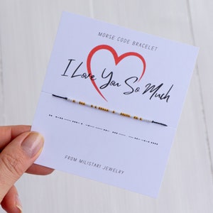 May include: A white card with a red heart and the text "I Love You So Much" in black. The card also has the text "Morse Code Bracelet" and "From Miliatari Jewelry". A black and white beaded bracelet is displayed on the card.