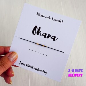May include: A black string bracelet with gold beads spelling out the word "Ohana" in Morse code. The bracelet is displayed on a white card with the text "Morse code bracelet Ohana from Milstarjewelry 2-5 DAYS DELIVERY".