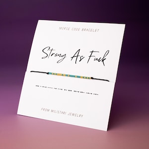 May include: A white card with black text that reads "Morse Code Bracelet" and "Strong As Fuck". A black string bracelet with blue and yellow beads is displayed on the card. The card also includes the text "From Milistasi Jewelry" and the Morse code for the phrase "Strong As Fuck".
