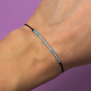 May include: A simple bracelet with a black cord and a row of light blue and silver beads.