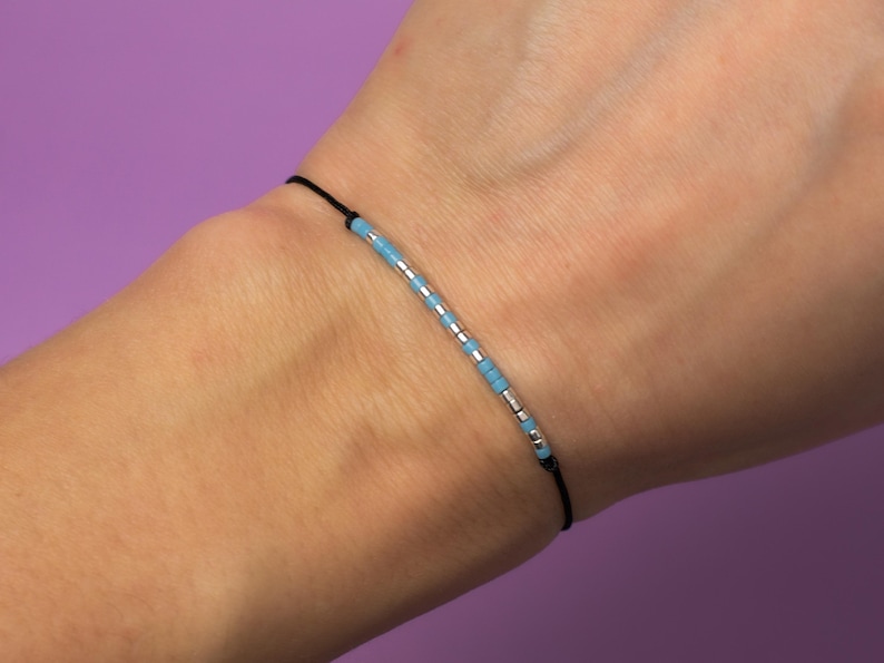 May include: A simple bracelet with a black cord and a row of light blue and silver beads.