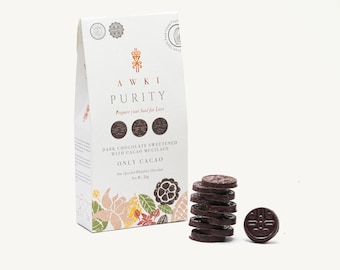 May include: A white rectangular package of Awki Purity dark chocolate sweetened with cacao mucilage, net weight 50g. The packaging features botanical illustrations and a stack of seven small, round, dark chocolate discs with embossed designs.