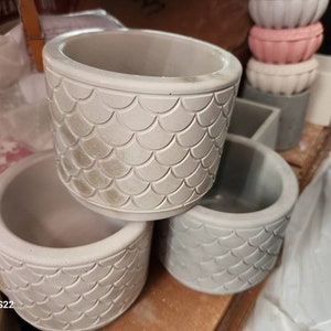 May include: Four gray concrete planters with a scale pattern. The planters are round and have a smooth, textured surface.