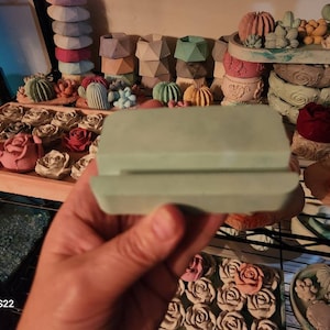 May include: A set of two light green concrete molds for making decorative concrete items. The molds are stacked on top of each other and are being held by a hand.