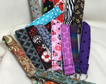 May include: A collection of 12 colorful fabric keychains with different patterns, including floral, polka dot, geometric, and animal print. The keychains are attached to silver key rings.