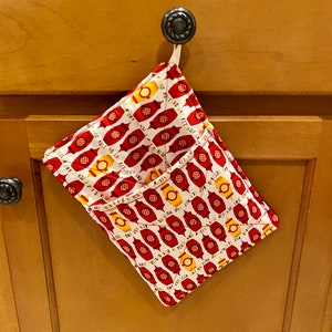 May include: A red and white kitchen towel with a pattern of mustard and ketchup bottles. The towel is hanging on a cabinet door handle.