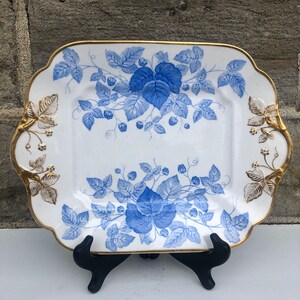 May include: A white square serving platter with a blue and gold floral design. The platter has a scalloped edge and gold accents.
