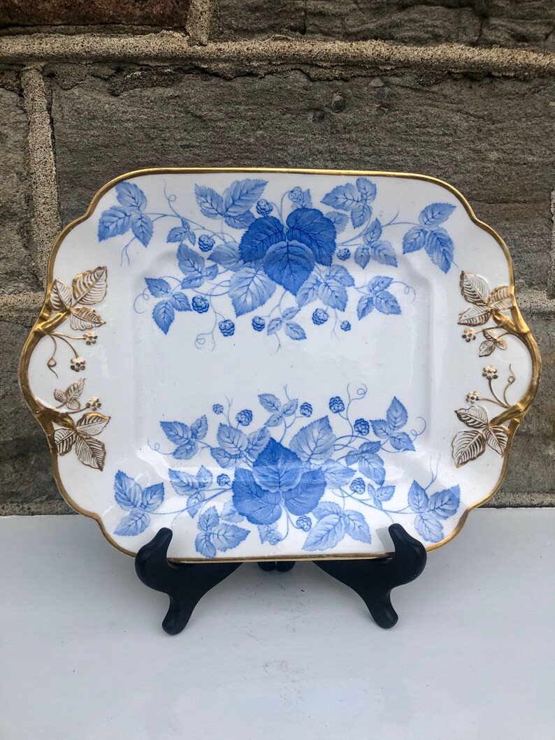 May include: A white square serving platter with a blue and gold floral design. The platter has a scalloped edge and gold accents.