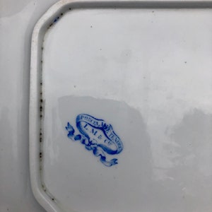 May include: A close-up of a blue and white porcelain mark on a white plate. The mark reads "Porcelain de Tendee L.M. & Cie."