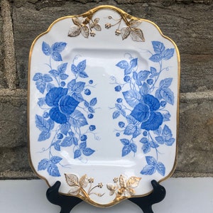 May include: A white rectangular serving platter with a blue and gold floral design. The platter has a scalloped edge and is decorated with a repeating pattern of blue leaves and berries with gold accents.