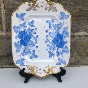 May include: A white porcelain serving platter with a blue and gold floral design. The platter has a scalloped edge and a gold trim.