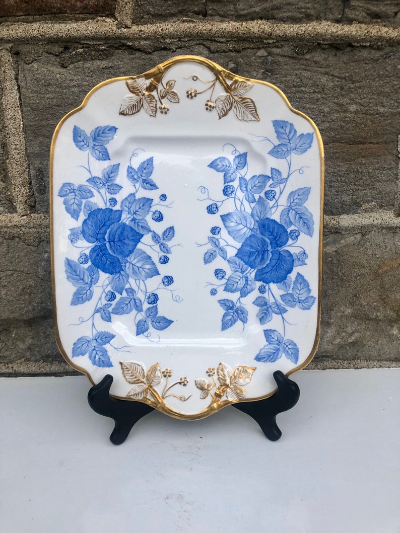 May include: A white porcelain serving platter with a blue and gold floral design. The platter has a scalloped edge and a gold trim.